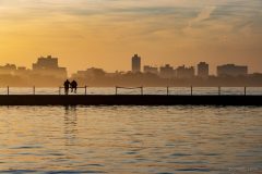 Silhouettes of two figures on Montrose Breakwater in Chicago during a hazy sunset. Fall 2020.